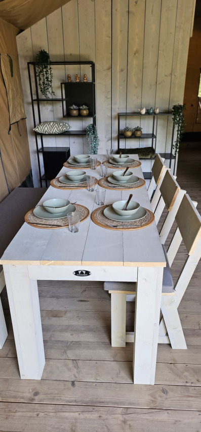 Table à manger dressée dans une tente safari avec vaisselle, étagères et murs en bois au Camping Reiler, Luxembourg.