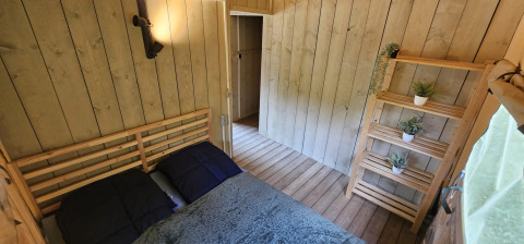 Soveværelse i safaritelt med dobbeltseng, trævægge og reol med planter på Camping Reiler, Luxembourg.