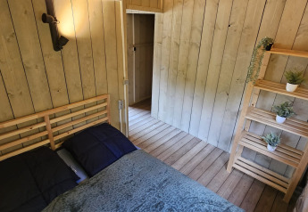 Dormitorio en tienda safari con cama doble, estantería y plantas decorativas en Camping Reiler, Luxemburgo.