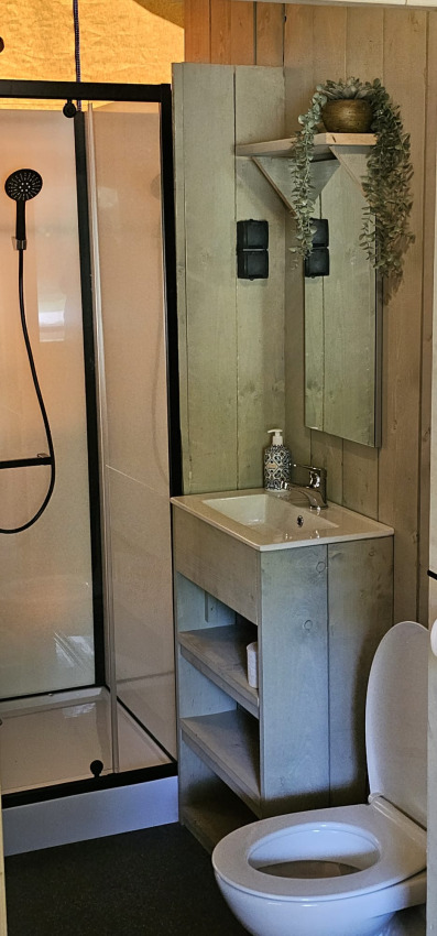 Badkamer met douche, wastafel, spiegel en toilet in een safaritent bij Camping Reiler in Luxemburg.