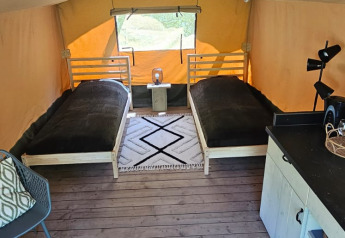 Indersiden af en safaritelte med to enkeltsenge, et lille bord, tæpper og træplankegulv på Camping Reiler.