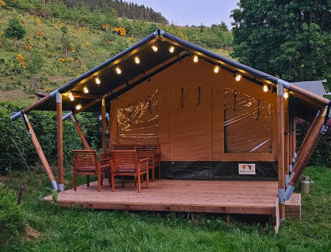 Tenda safari con veranda in legno, luci decorative e tavolo da esterno in un ambiente verde.