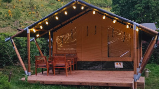 Safari-telt med træveranda, belysning og havemøbler, set i naturskønne grønne omgivelser.