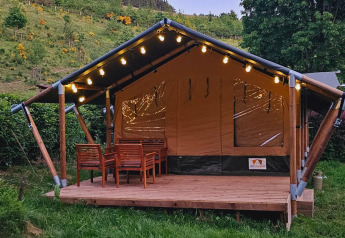 Tenda safari con veranda in legno, luci decorative e tavolo da esterno in un ambiente verde.