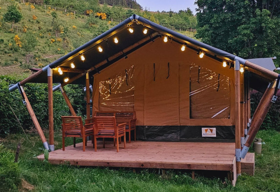 Tente safari avec terrasse en bois, guirlande lumineuse et meubles d’extérieur, en pleine nature.