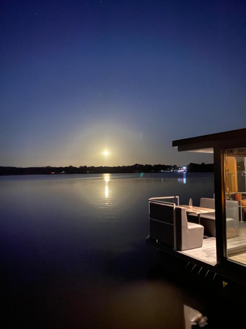 Evening photo from a houseboat showing calm water, moonlight, and a cozy outdoor dining area on the lake.