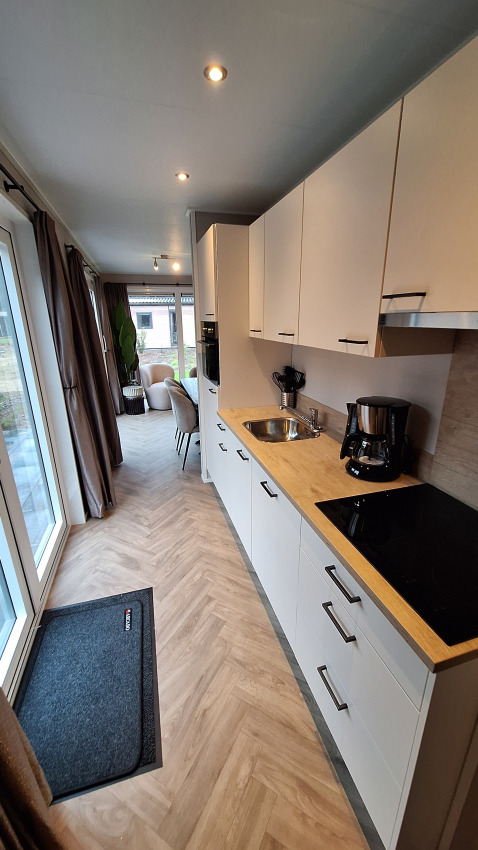 Moderne kitchenette met witte kasten in Groeneborg lodge te Vakantiepark De Wiltzangh, Nederland, zicht op living.