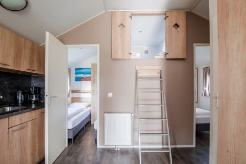 Interior de una cabaña con cocina, dormitorios y altillo con escalera en Vakantiepark Leukermeer, Países Bajos.