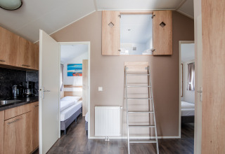 Intérieur d'un lodge avec cuisine, chambres et mezzanine accessible par une échelle à Vakantiepark Leukermeer, Pays-Bas.