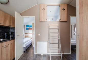 Interno di una lodge con cucina, camere e soppalco accessibile da scala a Vakantiepark Leukermeer, Paesi Bassi.