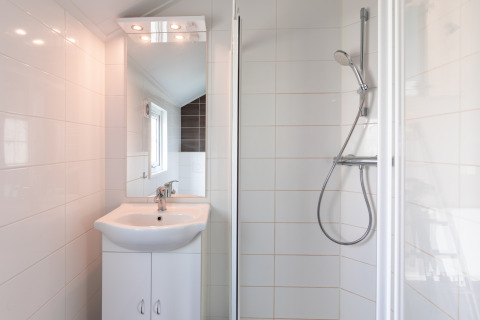 Modern bathroom with sink and shower at Lodge in Vakantiepark Leukermeer, Netherlands, white tiled walls.