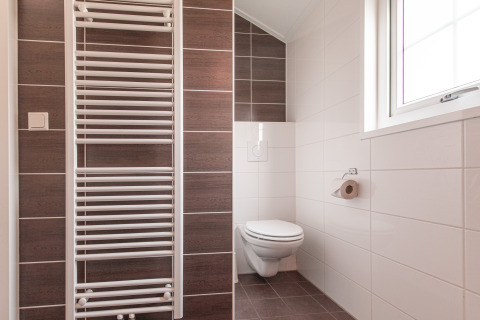 Moderne badkamer met hangend toilet, handdoekradiator en groot raam in Lodge bij Vakantiepark Leukermeer.