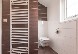 Moderne badkamer met hangend toilet, handdoekradiator en groot raam in Lodge bij Vakantiepark Leukermeer.