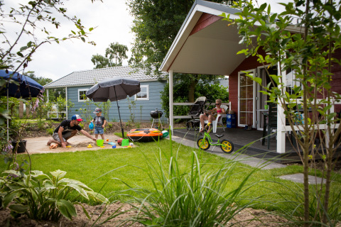 Familia disfruta de actividades al aire libre frente a una cabaña en Vakantiepark Leukermeer, Países Bajos, verano.