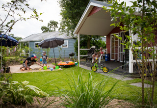 Gezin geniet van buitenactiviteiten voor een lodge in Vakantiepark Leukermeer, Nederland, zomerse dag.