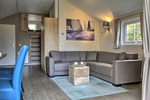 Salon moderne du Lodge au Vakantiepark Leukermeer, Pays-Bas, avec canapé d’angle et photo de voiliers.