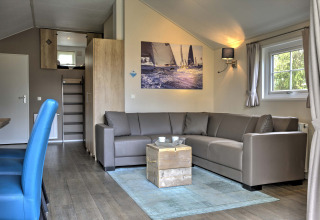 Moderne woonkamer in de Lodge op Vakantiepark Leukermeer, Nederland, met hoekbank en zeilfoto aan de muur.