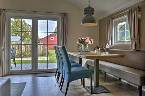 Eethoek met blauwe stoelen, bloemen op tafel en tuinzicht bij Lodge in Vakantiepark Leukermeer, Nederland.