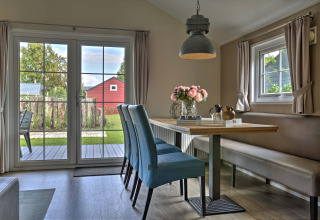 Eethoek met blauwe stoelen, bloemen op tafel en tuinzicht bij Lodge in Vakantiepark Leukermeer, Nederland.