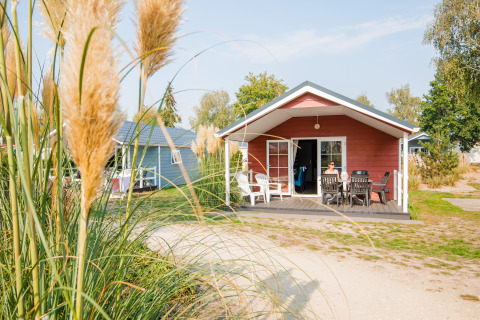 Rode lodge bij Vakantiepark Leukermeer in Nederland met veranda en tuin, persoon geniet buiten van het weer.