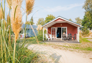 Rode lodge bij Vakantiepark Leukermeer in Nederland met veranda en tuin, persoon geniet buiten van het weer.