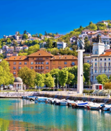 Hermoso paseo marítimo de Krk, Croacia, con barcos amarrados, casas en colina y una estatua central.