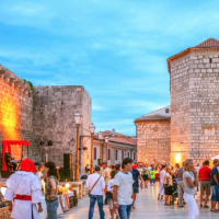 Personas pasean por Krk, Croacia, admirando murallas de piedra antiguas y edificios históricos iluminados.