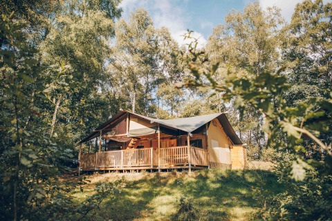 Safarizelt mit überdachter Veranda mitten im Wald, umgeben von grünen Bäumen und Natur.