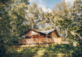 Safarizelt mit überdachter Veranda mitten im Wald, umgeben von grünen Bäumen und Natur.