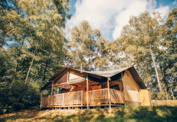 Safaritent bij Wilsumer Berge in Duitsland, met houten veranda en omgeven door bomen en blauwe lucht.