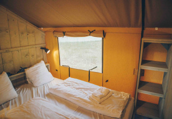 Gemütlicher Innenraum eines Safari-Zeltes mit Doppelbett und Regal bei Wilsumer Berge, Deutschland.