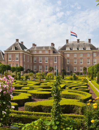 Majestuosa mansión con bandera holandesa y jardines decorativos en un parque de vacaciones glamping.