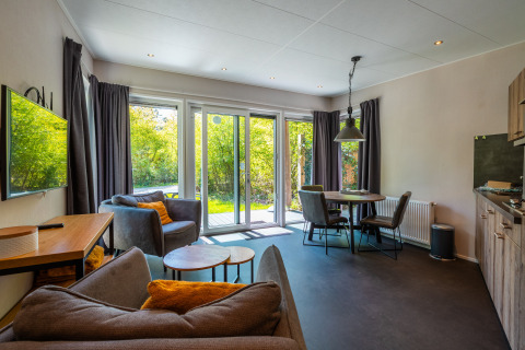 Soggiorno accogliente con grandi finestre e zona pranzo in Wellness Lodge a De Wiltzangh, Paesi Bassi.