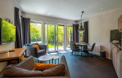 Soggiorno accogliente con grandi finestre e zona pranzo in Wellness Lodge a De Wiltzangh, Paesi Bassi.