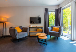 Moderne stue i Wellness Lodge på Vakantiepark De Wiltzangh, Nederlandene, med store vinduer og komfortable stole.