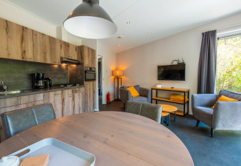 Modernes Wohnzimmer und Küche in der Wellness Lodge im Vakantiepark De Wiltzangh, Niederlande, mit Sofa und TV.
