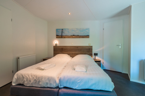 Chambre avec deux lits simples, tête de lit en bois et tableau de paysage au Wellness Lodge à De Wiltzangh, Pays-Bas.