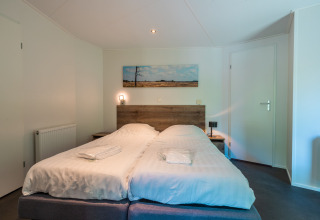Dormitorio con dos camas individuales, cabecero de madera y cuadro de paisaje en Wellness Lodge, De Wiltzangh, Países Bajos.