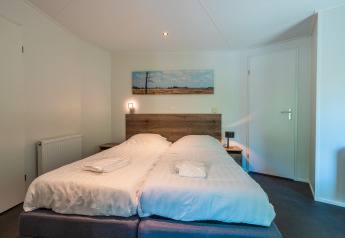 Dormitorio con dos camas individuales, cabecero de madera y cuadro de paisaje en Wellness Lodge, De Wiltzangh, Países Bajos.