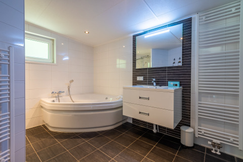 Moderne badeværelse med hjørnebadekar, stor spejl, håndvask og radiator i Wellness Lodge, De Wiltzangh.