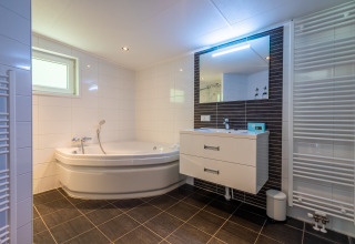 Bagno moderno con vasca ad angolo, lavabo, grande specchio e termosifone presso Wellness Lodge, De Wiltzangh.