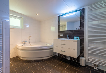 Baño moderno con bañera de esquina, lavabo, gran espejo y radiador en Wellness Lodge, De Wiltzangh.