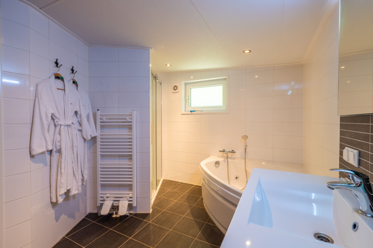 Helles Badezimmer mit Whirlpool, Waschbecken, Bademänteln und Fenster in der Wellness Lodge De Wiltzangh.