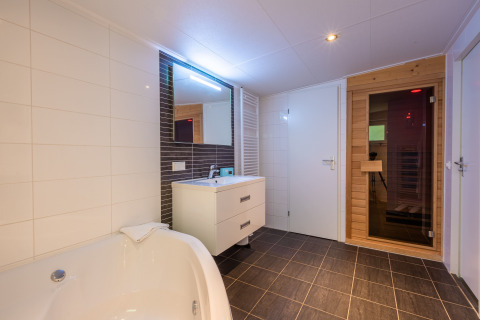 Baño moderno en Wellness Lodge con bañera, lavabo, espejo y sauna en Vakantiepark De Wiltzangh, Países Bajos.