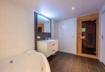 Moderne badeværelse i Wellness Lodge med badekar, vask, spejl og sauna i Vakantiepark De Wiltzangh.
