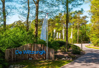 Entrée de la Wellness Lodge au Vakantiepark De Wiltzangh aux Pays-Bas, entourée d’arbres verts luxuriants.