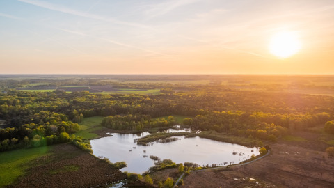 Vue aérienne de la Wellness Lodge au Vakantiepark De Wiltzangh aux Pays-Bas avec coucher du soleil sur lac et forêt.