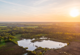 Vue aérienne de la Wellness Lodge au Vakantiepark De Wiltzangh aux Pays-Bas avec coucher du soleil sur lac et forêt.