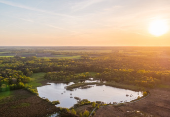 Vista aerea di Wellness Lodge al Vakantiepark De Wiltzangh nei Paesi Bassi con il sole che tramonta su lago e foresta.