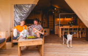 Couple profitant du vin sur la terrasse d’une Safarilodge Gazelle avec leur chien au Vakantiepark IJsselhof.